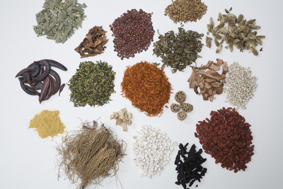 Hand scale with dried Chinese herbs in front of apothecary jars