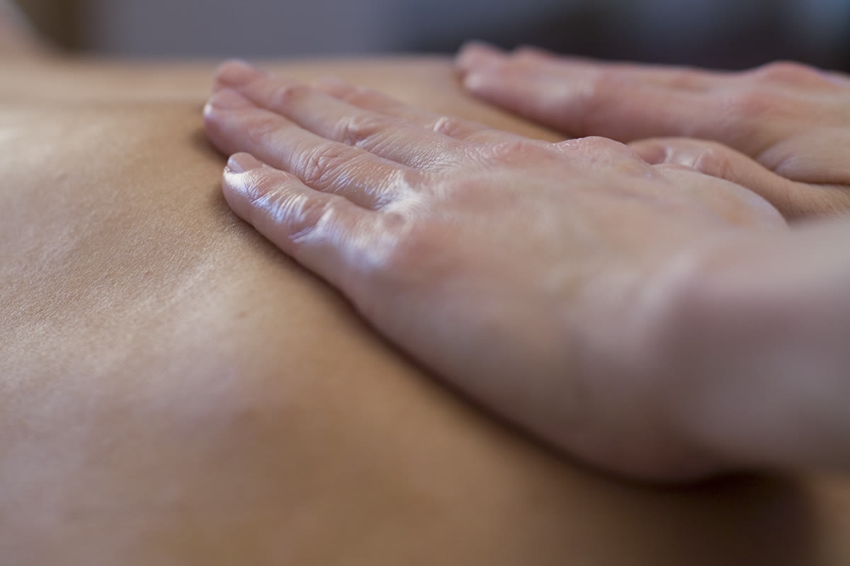 Two hands massaging the shoulder and neck of a person lying down